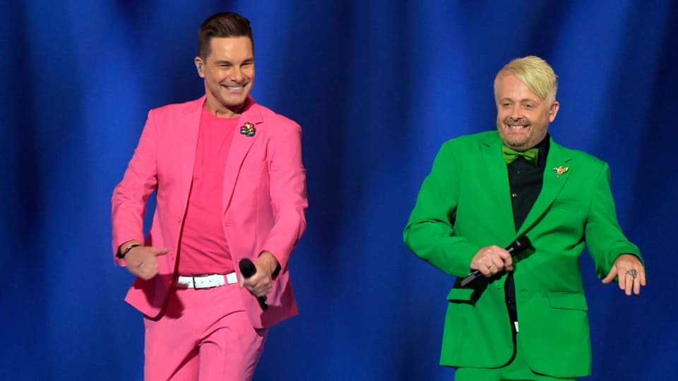 Eloy in pinkfarbenem und Ross in grünem Anzug. 