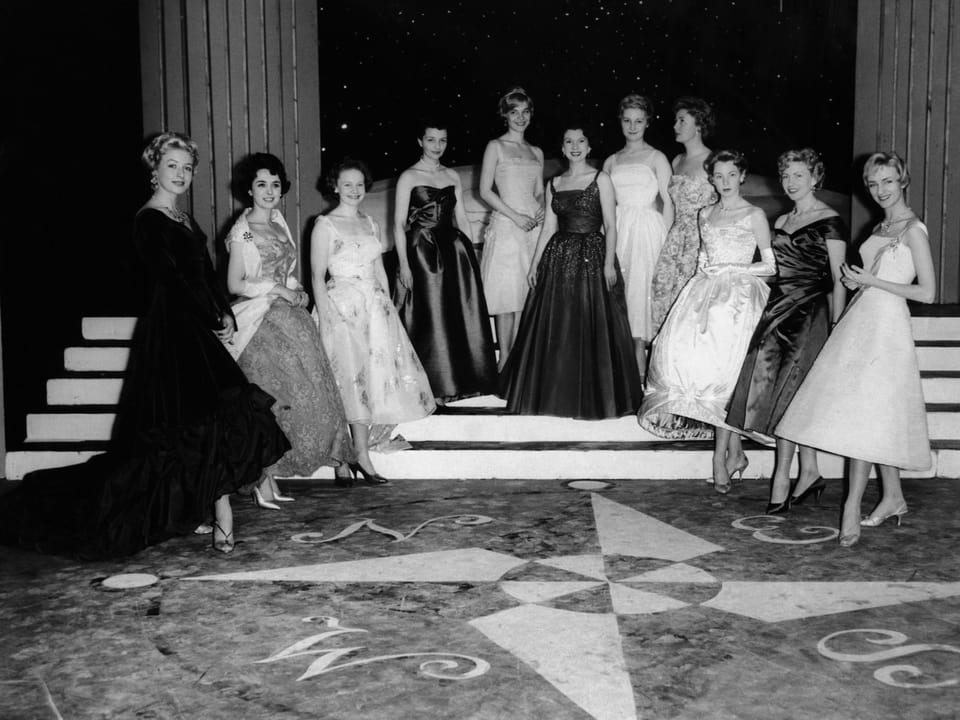 Elf Frauen in langen Roben posieren auf einer Treppe.