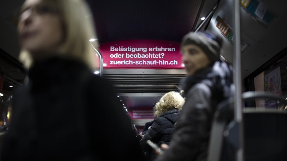 Personen stehen im Bus in Zürich, im Hintergrund ein Plakat von «Zürich schaut hin».