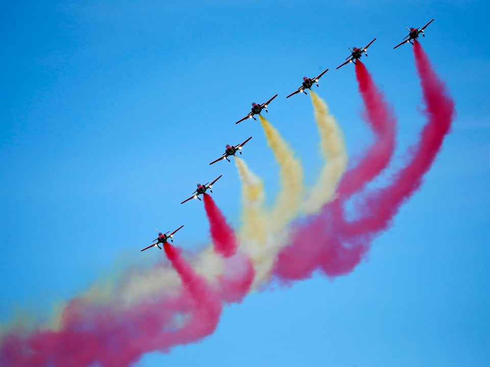 Blauer Himmel mit 7 Jets der Spanischen Kunstflugstaffel. Sie haben farbigen Rauch: Ein Streifen rot, dann weiss, dann wieder rot. 
