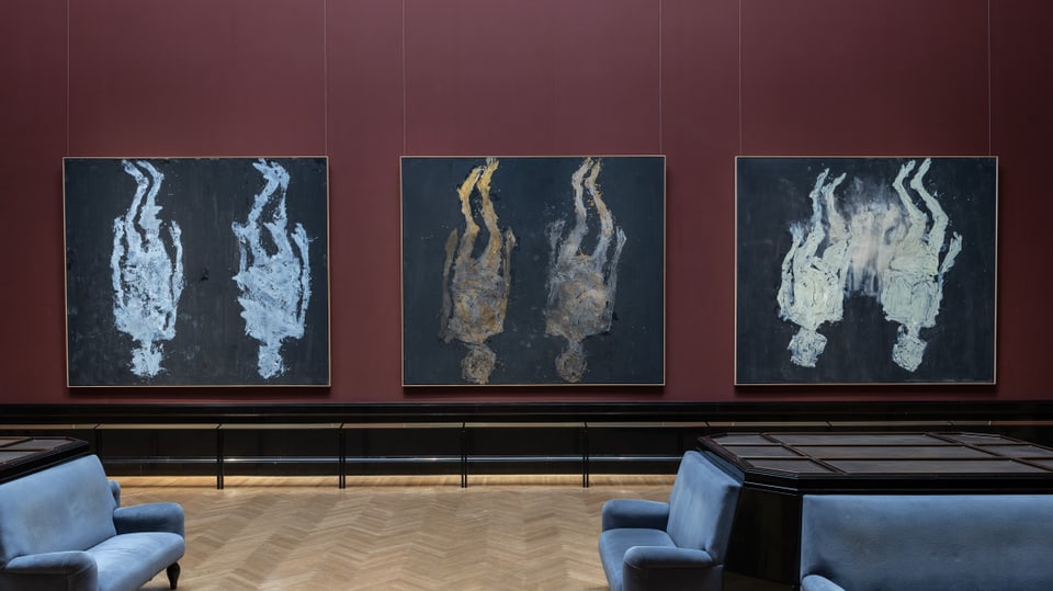 Drei Gemälde von Georg Baselitz hängen an einer grossen roten Wand im Museum.