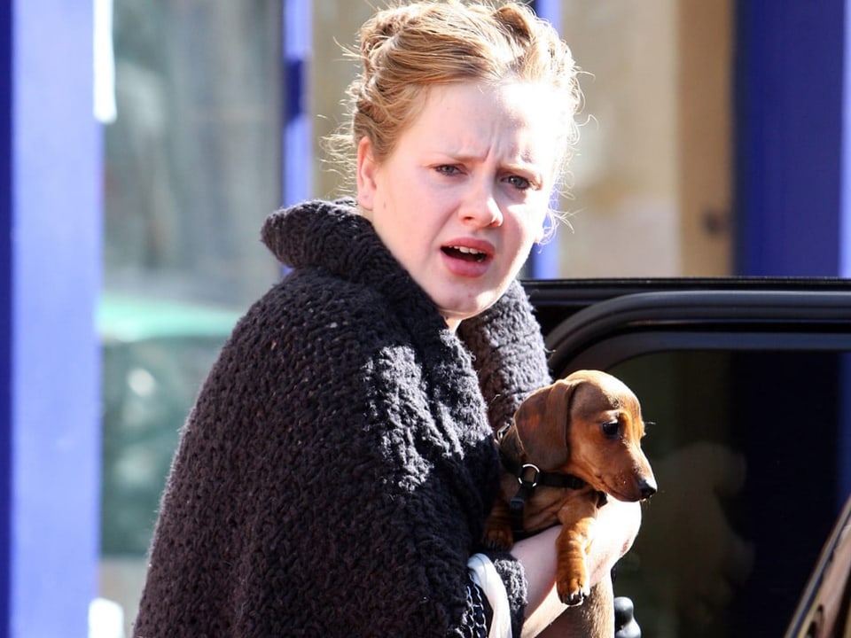 Adele mit Dackel im Arm auf der Strasse.