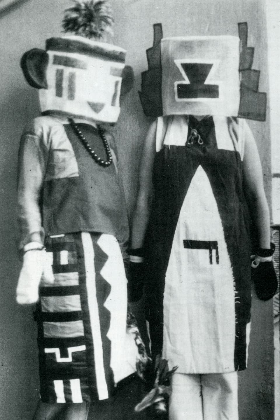 Zwei Figuren in Kostümen mit geometrischen Mustern, komplett verkleidete mit Maske.