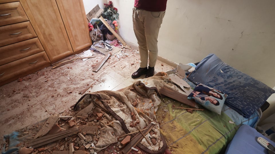 Schlafzimmer mit zerstörtem Bett und Boden, Person steht daneben.