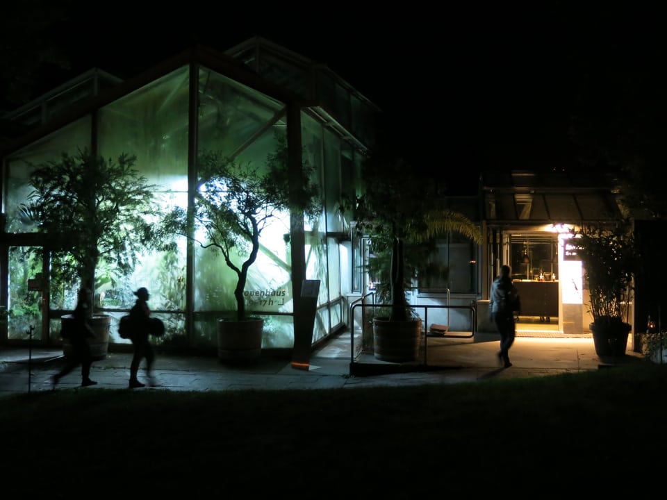 Beleuchtetes Tropenhaus, davor Silhouette von Besuchern