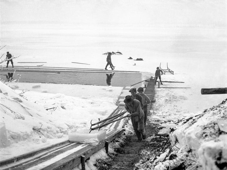 Menschen transportieren Schlitten an einem verschneiten Seeufer.