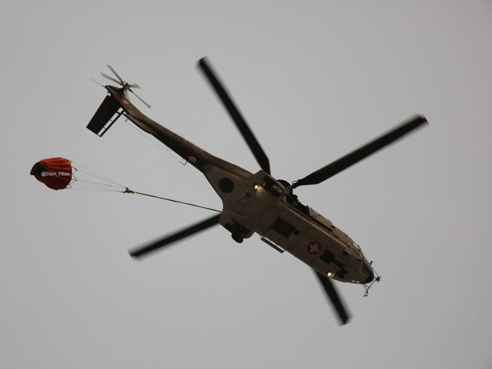 In der Luft fliegt ein Helikopter. An einem Seil ist ein Sack befestigt.