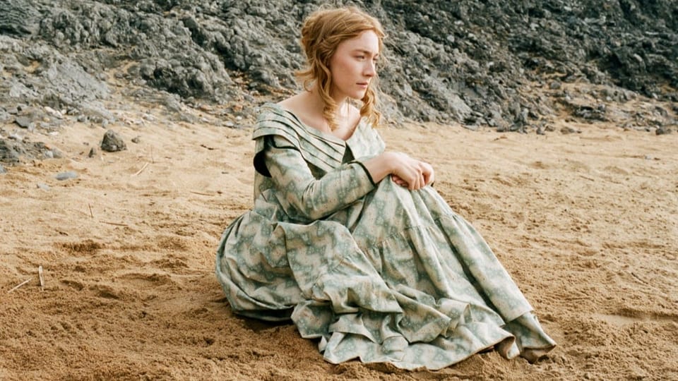 Saoirse Ronan, kostümiert als Charlotte, sitzt an einem Strand Südenglands.