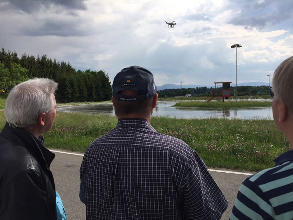 Drei Männer beobachten eine fliegende Drohne.