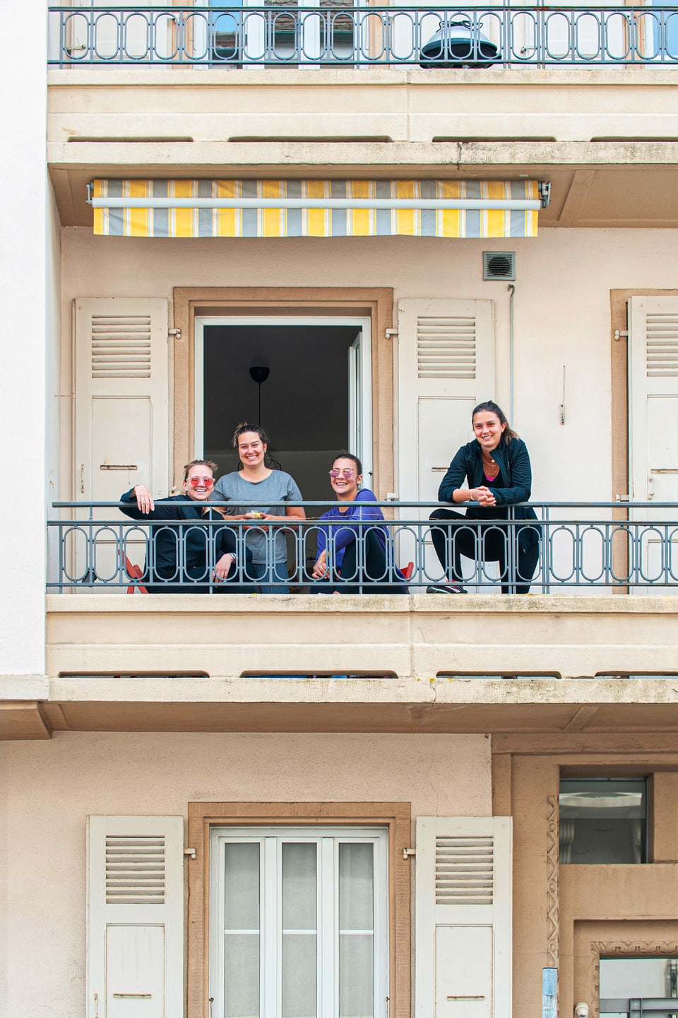 Vier junge Frauen stehen und sitzen auf einem Balkon.