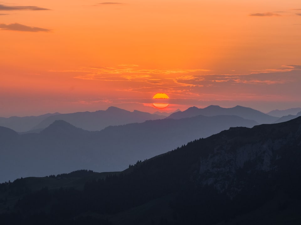 Roter Sonnenaufgang hinter bläulichen Bergen.