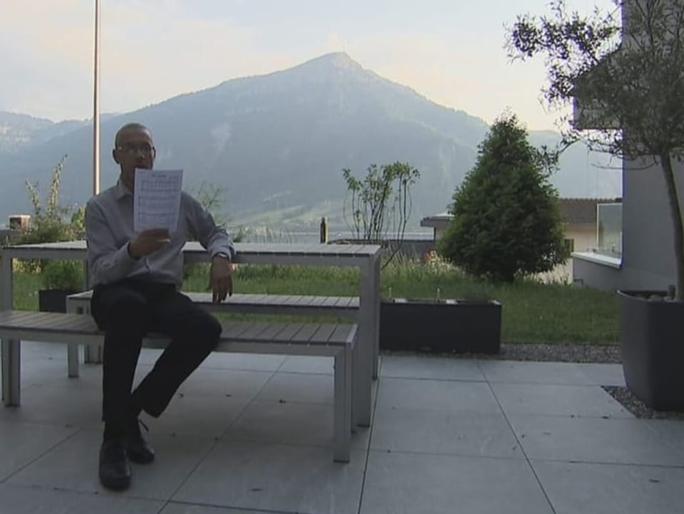 Mann sitzt an einer Bank auf einer Terrasse.