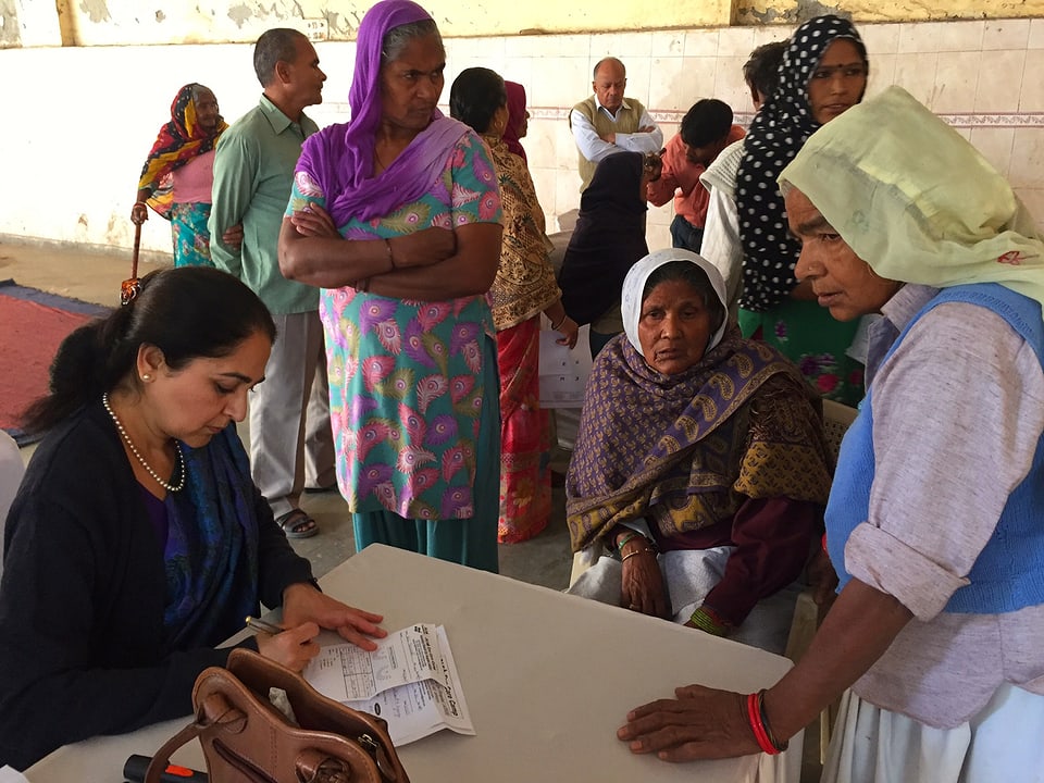 Eine Augenärztin füllt ein Formular aus, um ihren Tisch stehen Frauen aus dem Dorf.