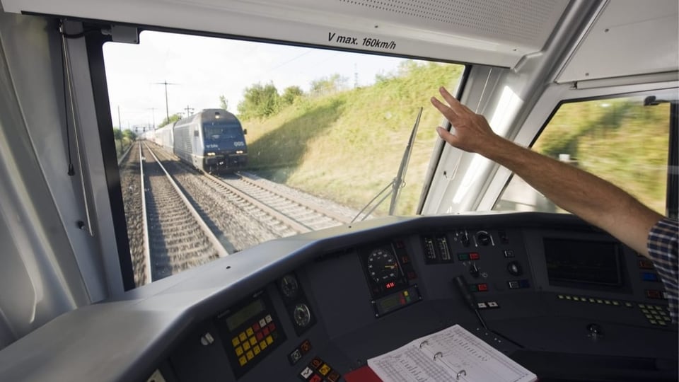 Lokführer grüsst mit erhobener hand vorbeifahrenden Zug auf der Gegenstrecke.