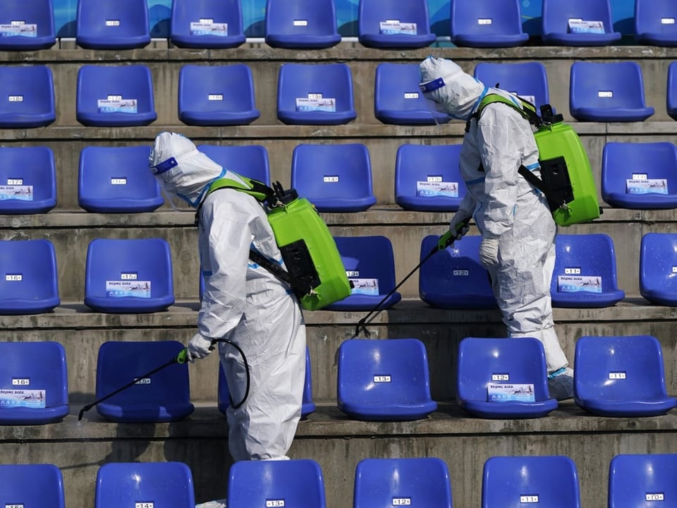 Zwei Personen in Schutzanzügen desinfizieren die Sitze in einem Stadion.