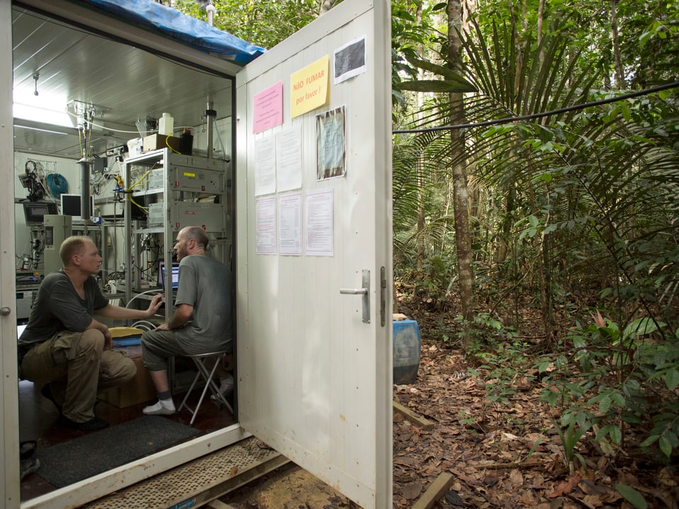 Zwei Forscher sitzen im Dschungel in einem Häuschen der Messstation