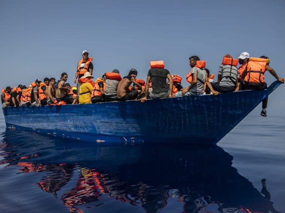 Boot mit über einem Dutzend Menschen an Bord (in Rettungswesten) treibt auf dem Meer