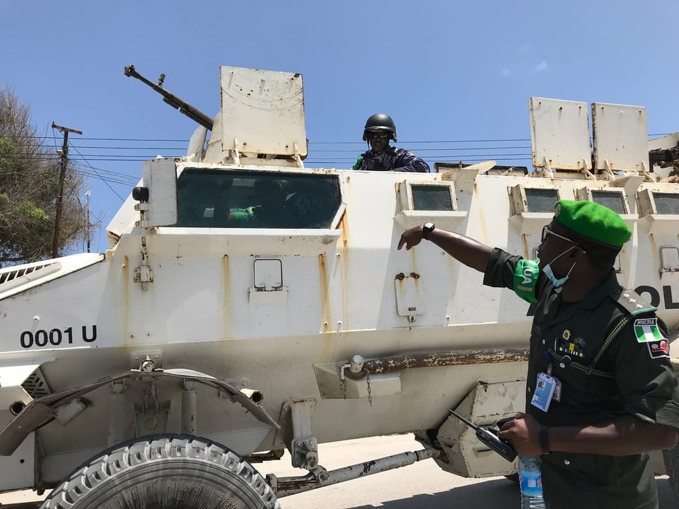 Ein hoher Militär in Uniform steht neben einem bewaffneten Truppenfahrzeug und gibt Anweisungen. 