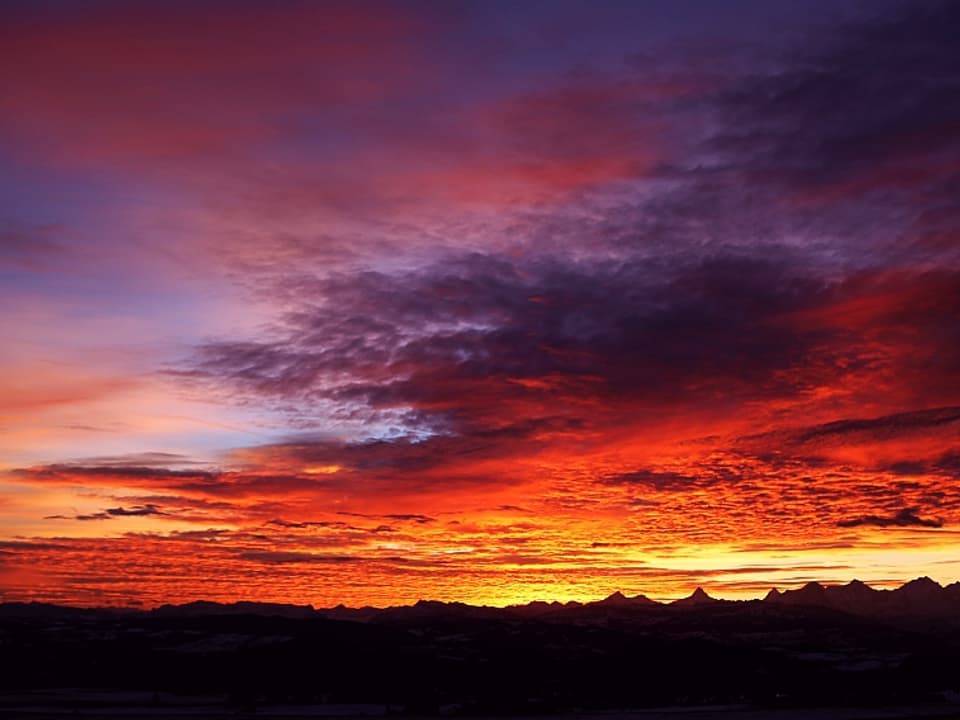Die Wolkenfelder am Morgenhimmel leuchten in lauter rot, orange, violet Tönen während die Kulisse der Berner Riesen (Eiger, Mönch und Jungfrau) noch im Schatten der Nacht verborgen sind.