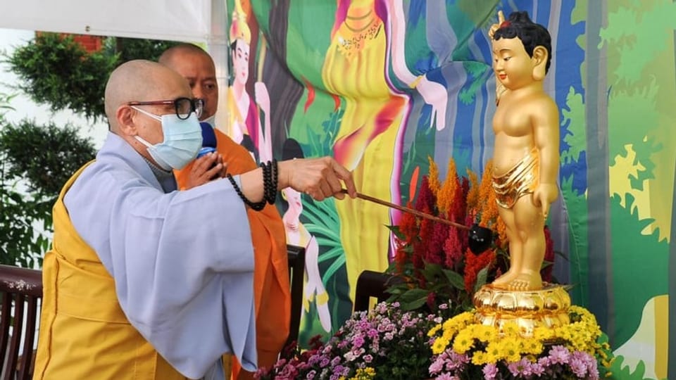 Ein Mönch giesst mit einer Kelle Wasser auf eine Statue