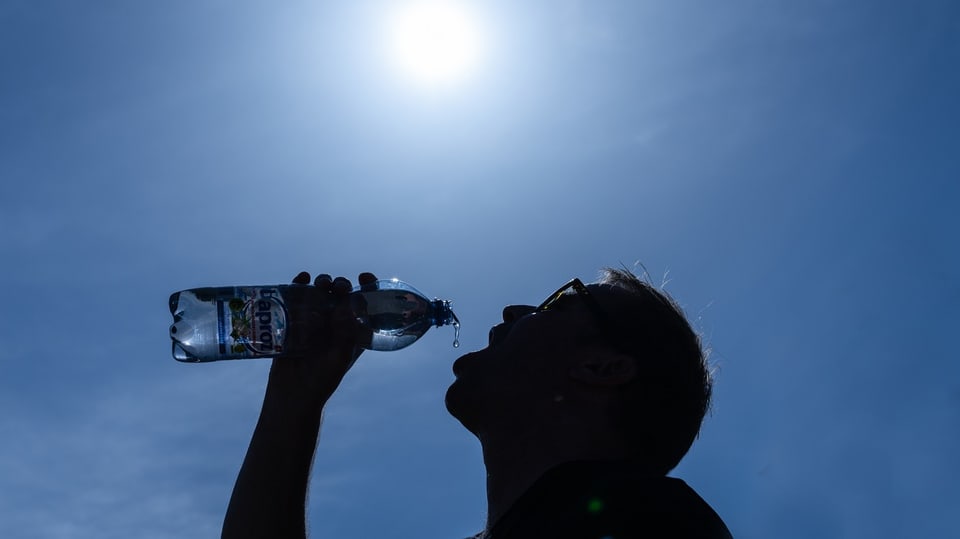 Mann nimmt Schluck aus der Wasserflasche. Über ihm: Die gleissende Sonne