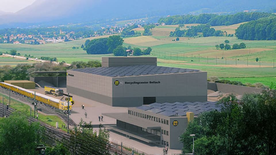 Bildmontage der fertigen Anlage. Sie steht gleich neben der Bahnlinie Solothurn-Grenchen, auf der Seite des Juras. Es ist ein grauer, grosser Bau, der aus mehreren Gebäudeteilen besteht. 