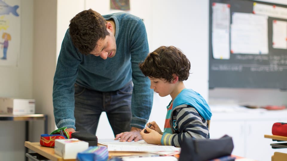 Ein Primarlehrer erklärt einem Schüler eine Aufgabe.