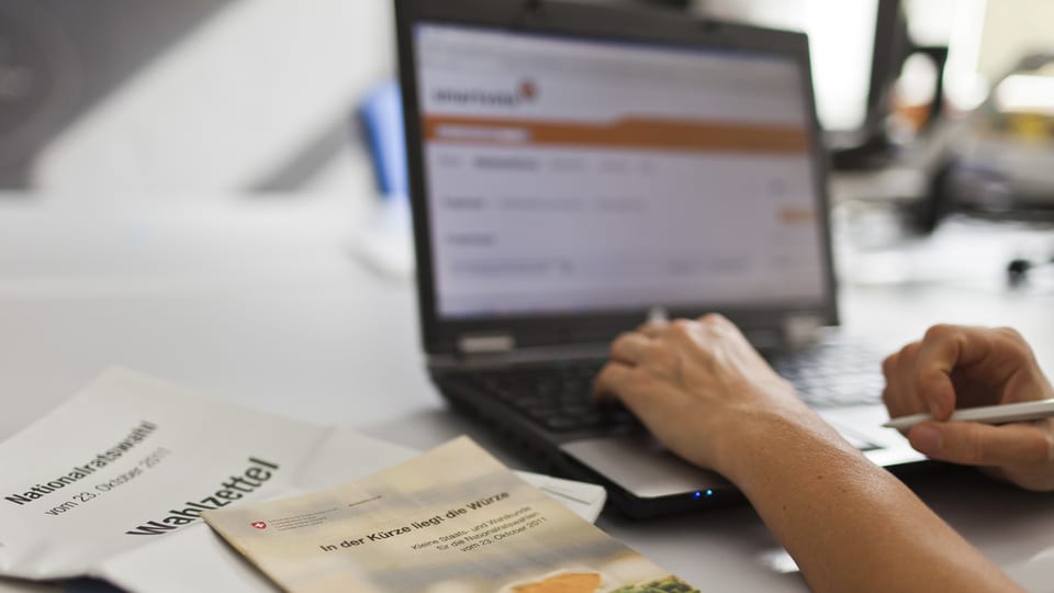 Ein Laptopbildschirm zeigt die Webseite von Smartvote, daneben liegen Wahlunterlagen.