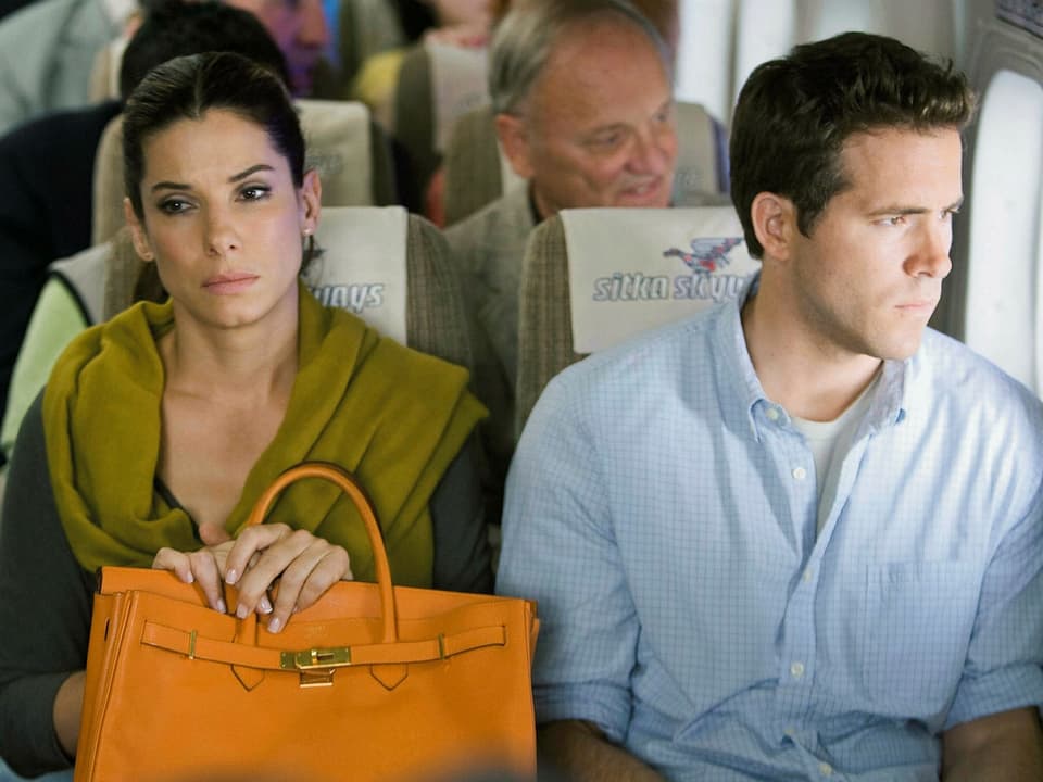Sandra Bullock und Ryan Reynolds sitzen verstimmt nebeneinander im Flugzeug und starren in die Leere.