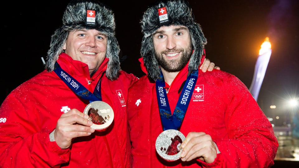 Beat Hefti (links) und Alex Baumann tragen wärmende Mützen und zeigen ihre Medaillen.
