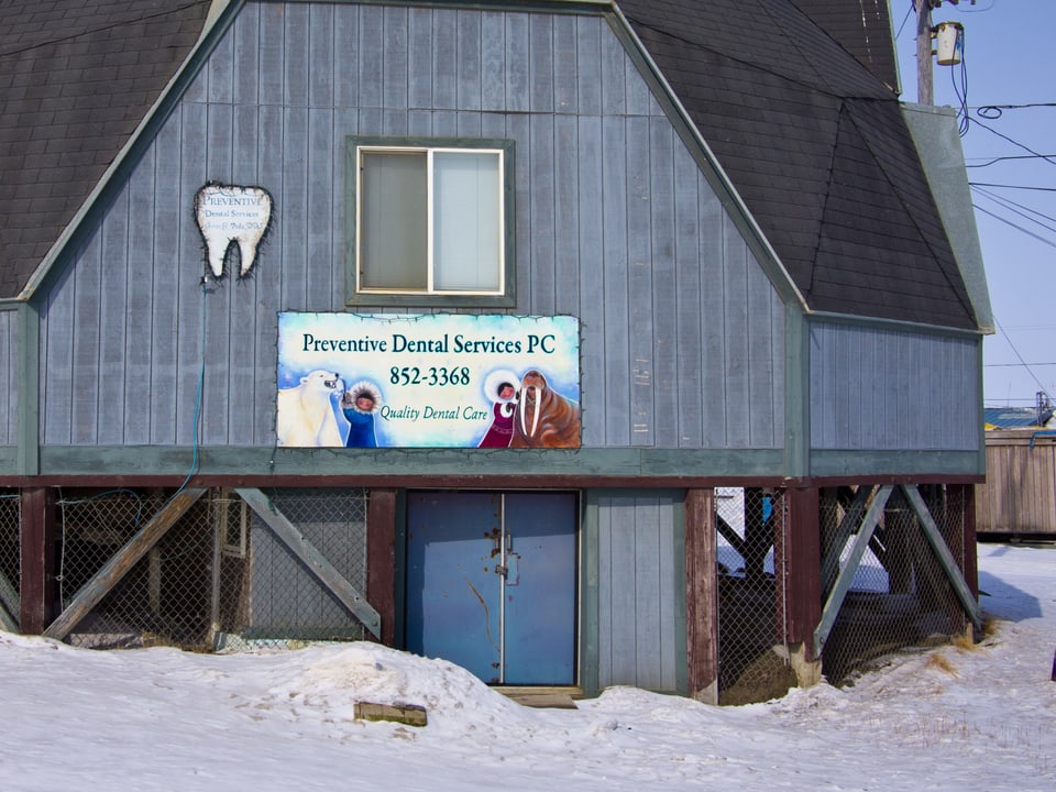 Ein Haus mit Schild, auf dem ein Zahnarzt für sich wirbt, zu sehen sind darauf zwei Kinder, eines mit Eisbär, das andere mit Walross im Arm.