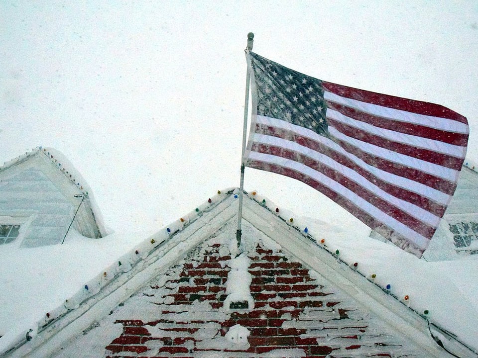 Schneebedeckte US-Fahne an Hausfassade.