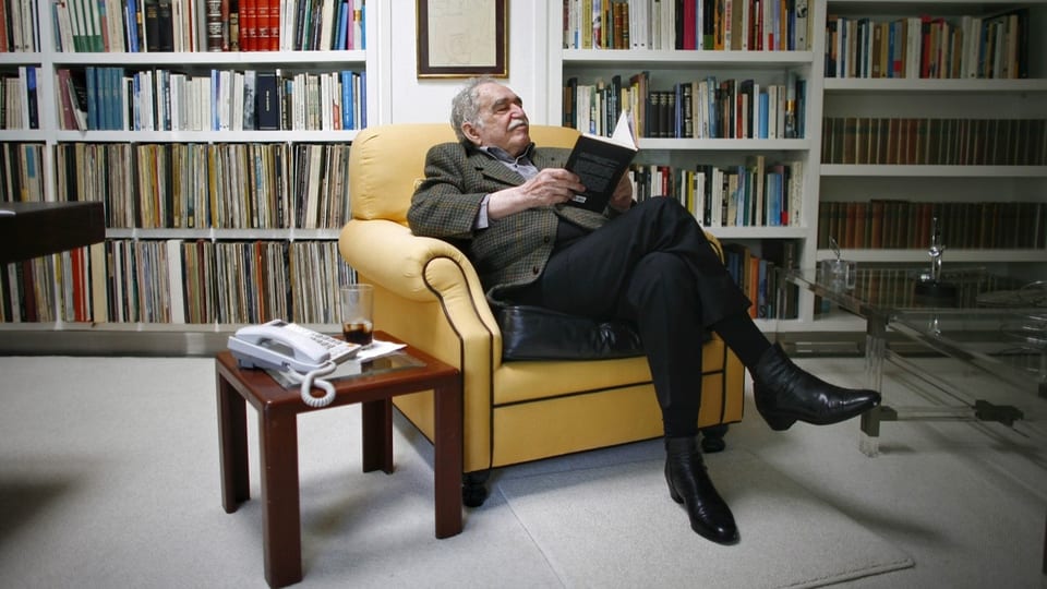 Der Autor Gabriel Garcia Marquez sitzt in seinem Wohnzimmer auf einem gelben Sessel und liest in einem Buch.
