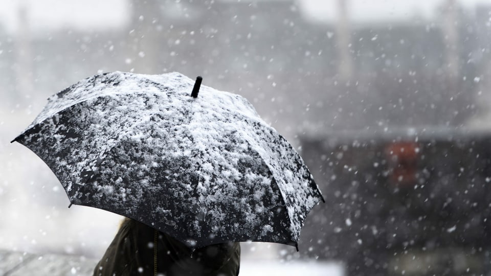 Eine Person mit einem schneebedeckten Schirm.