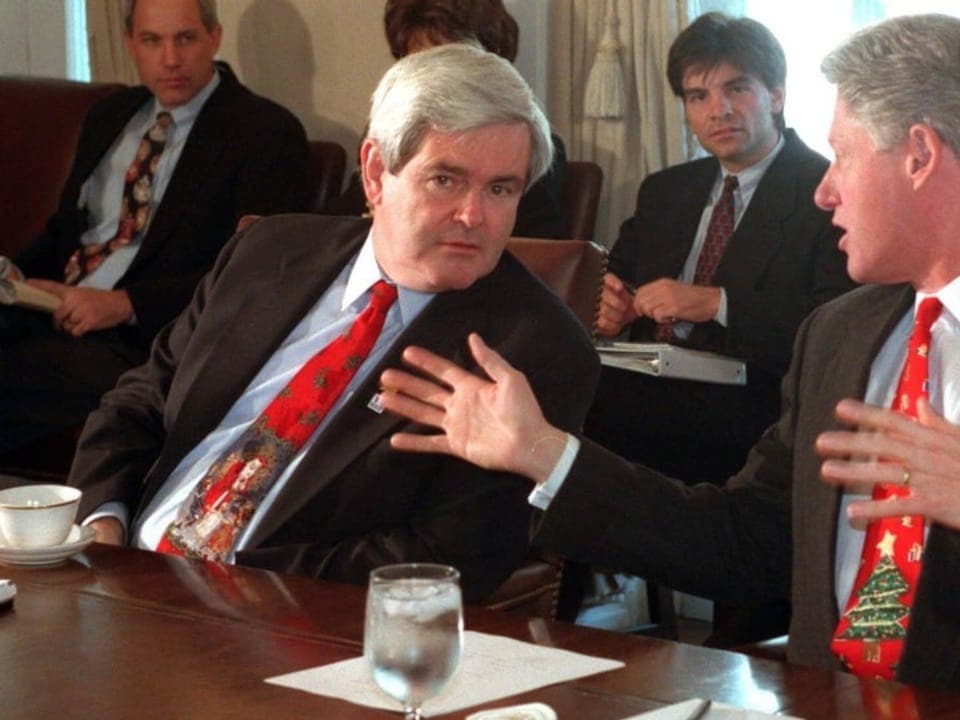 Newt Gingrich und Bill Clinton sitzen an Tisch nebeneinander und sind in Gespräch vertieft.