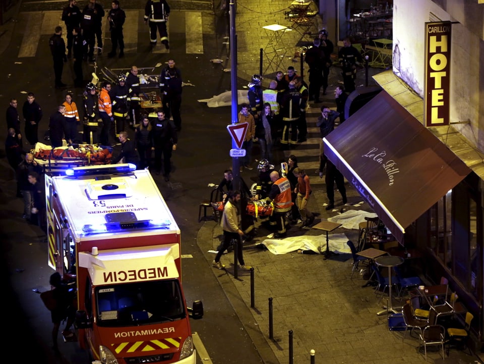 Das Bild zeigt Verletzte und Einsatzkräfte vor der Bar «Carillon», die an den Tatort angrenzt.