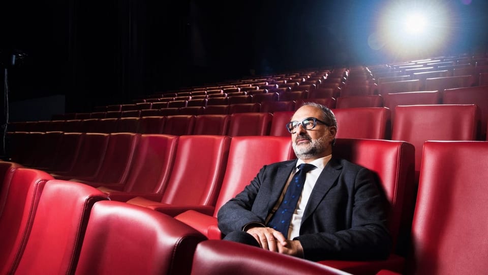 Ein Mann mit Brille und Anzug sitzt in einem leeren Kino.