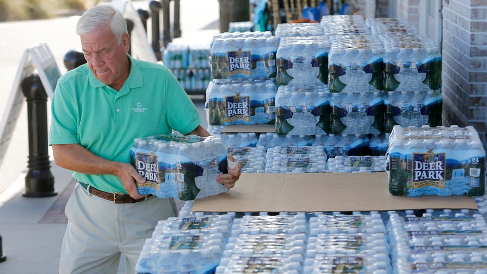 Älterer Mann nimmt 24-er Packung Halbliter-Wasserflaschen vom Stapel.