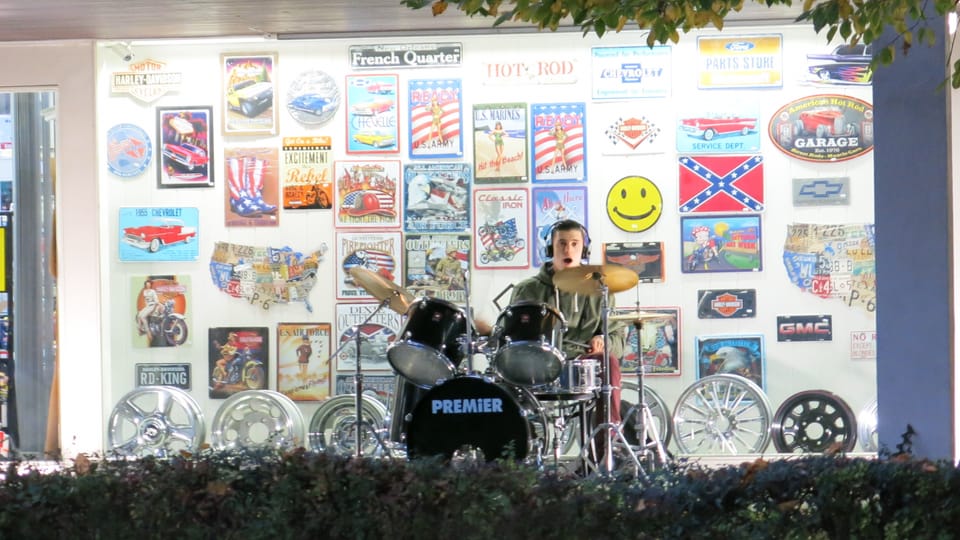 Ein junger Mann spielt Schlagzeug, vor einem Schaufenster.