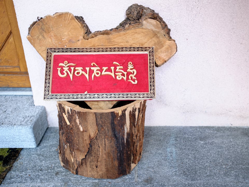 Ein rotes Schild mit indischem Schriftzug steht auf einem Holzpflock vor der Eingangstüre.