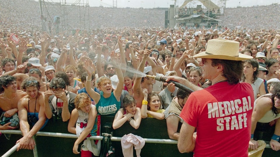 Ein Mann mit einem T-Shirt Medical Staff spritzt Wasser in eine riesige Publikumsmenge.
