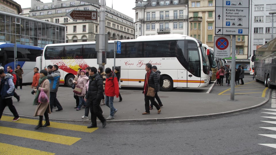 Touristen überqueren die Strasse beim Löwenplatz Luzern. Im Hintergrund sind Reisecars parkiert.
