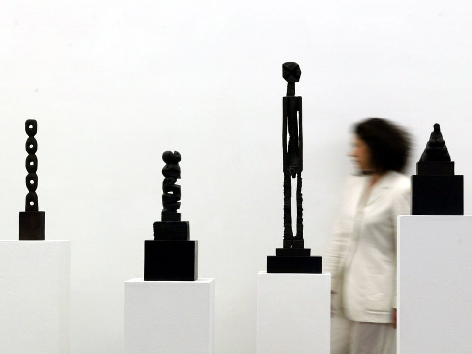 Frau geht an vier abstrakten Bronzefiguren vorbei.