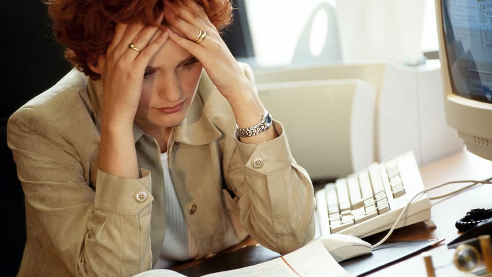 Eine Frau sitzt an ihrem Computer, den Kopf in die Hände gestützt.
