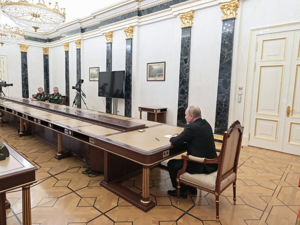 Gerassimow und Schoigu sitzen an einem langen Tisch, an dessen Ende Staatspräsident Putin sitzt.