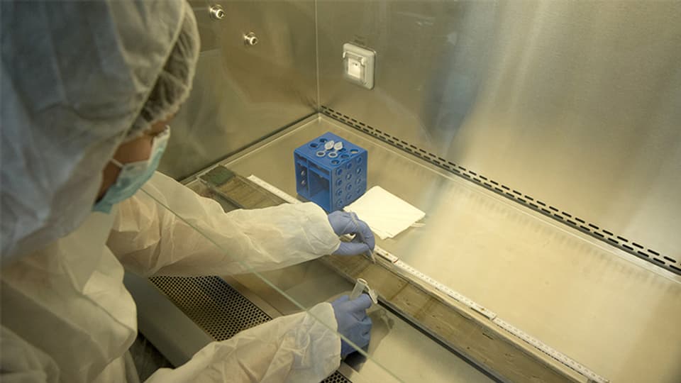 Eine Laborantin arbeitet unter sterilen Bedingungen mit einer Pipette und einem kleinen Behälter in der Hand.