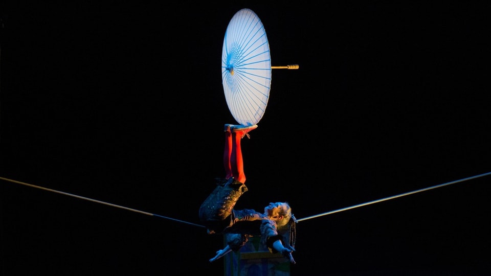 Eine Akrobation bei einer Theateraufführung liegt auf einem Seil und balanciert einen Schirm auf ihren Füssen.