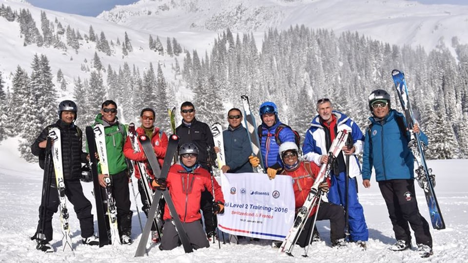 Acht nepalesische Skilehrer und ihre zwei Ausbildner vor dem verschneiten Alpenpanorama.