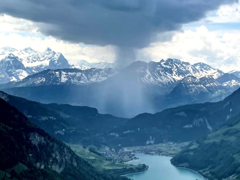 Alpenlandschaft mit dunklen Wolken und einem kleinen See. Am Horizont geht lokal Regen nieder. 