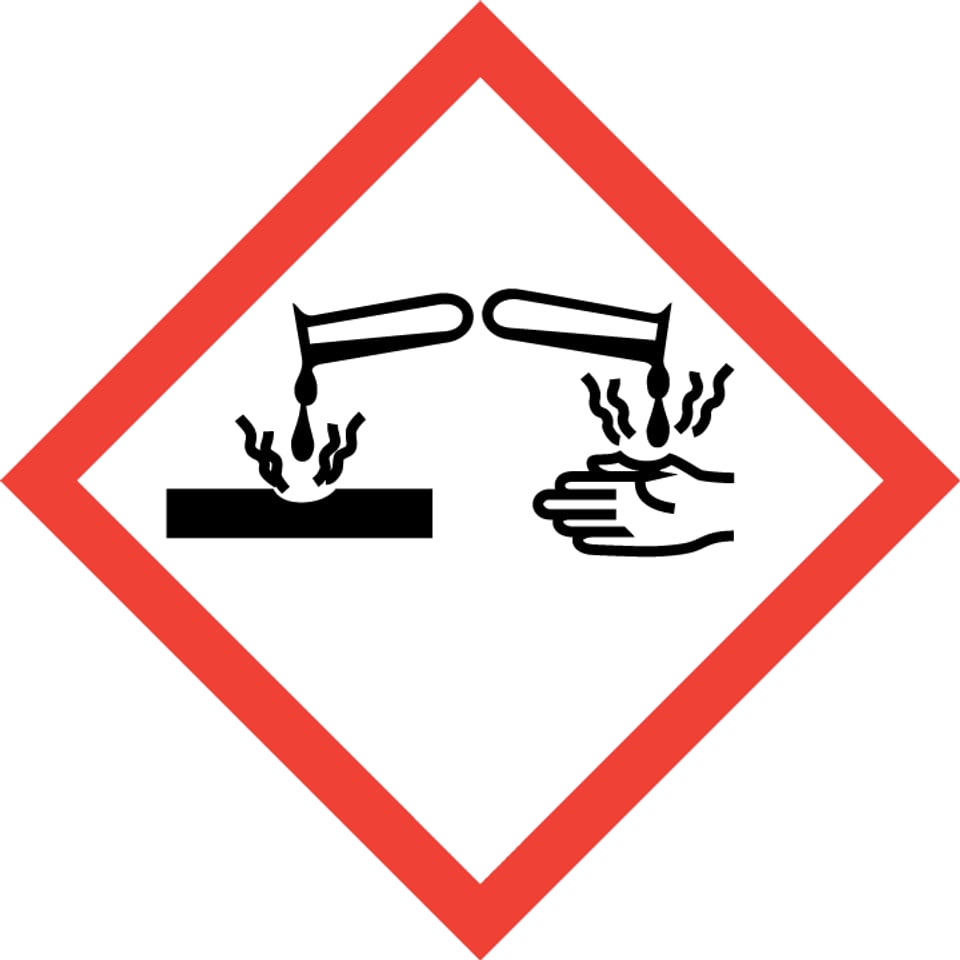 Gefahrenzeichen: Flüssigkeit tropft aus Laborglas auf Hand und Material und löst beides auf.
